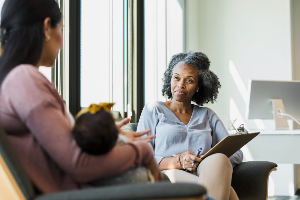 As the unrecognizable mid adult new mother shares, the mature adult female therapist listens patiently.